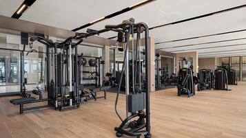 Un gimnasio moderno con diverso equipo de ejercicio, amplias ventanas y suelo de madera.