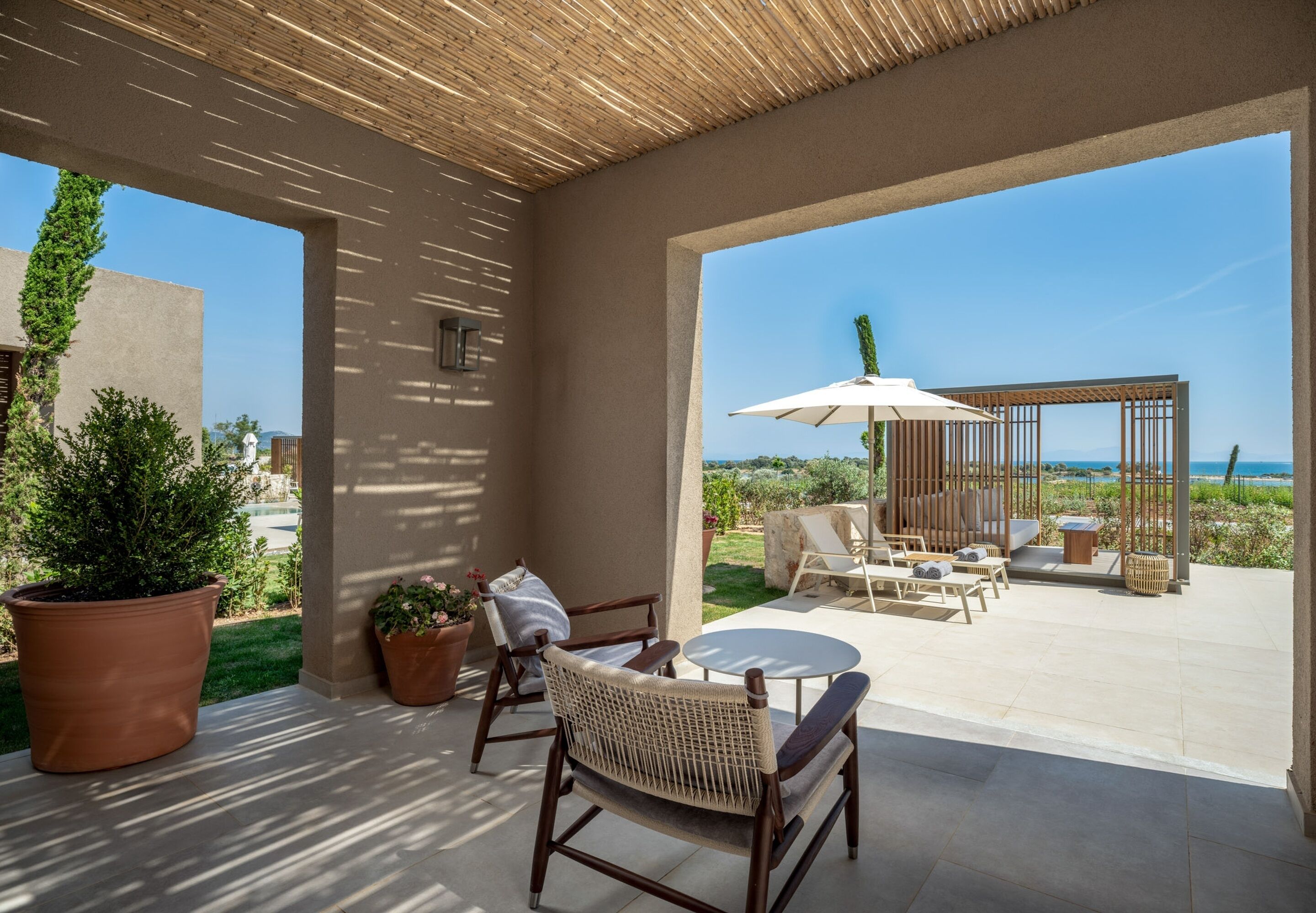 Un porche cubierto con mobiliario exterior, vista al mar y plantas en macetas.