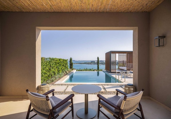 A poolside area with a view of the sea, a table, and wicker chairs. - Akra Didim Resort & SPA (Didim)