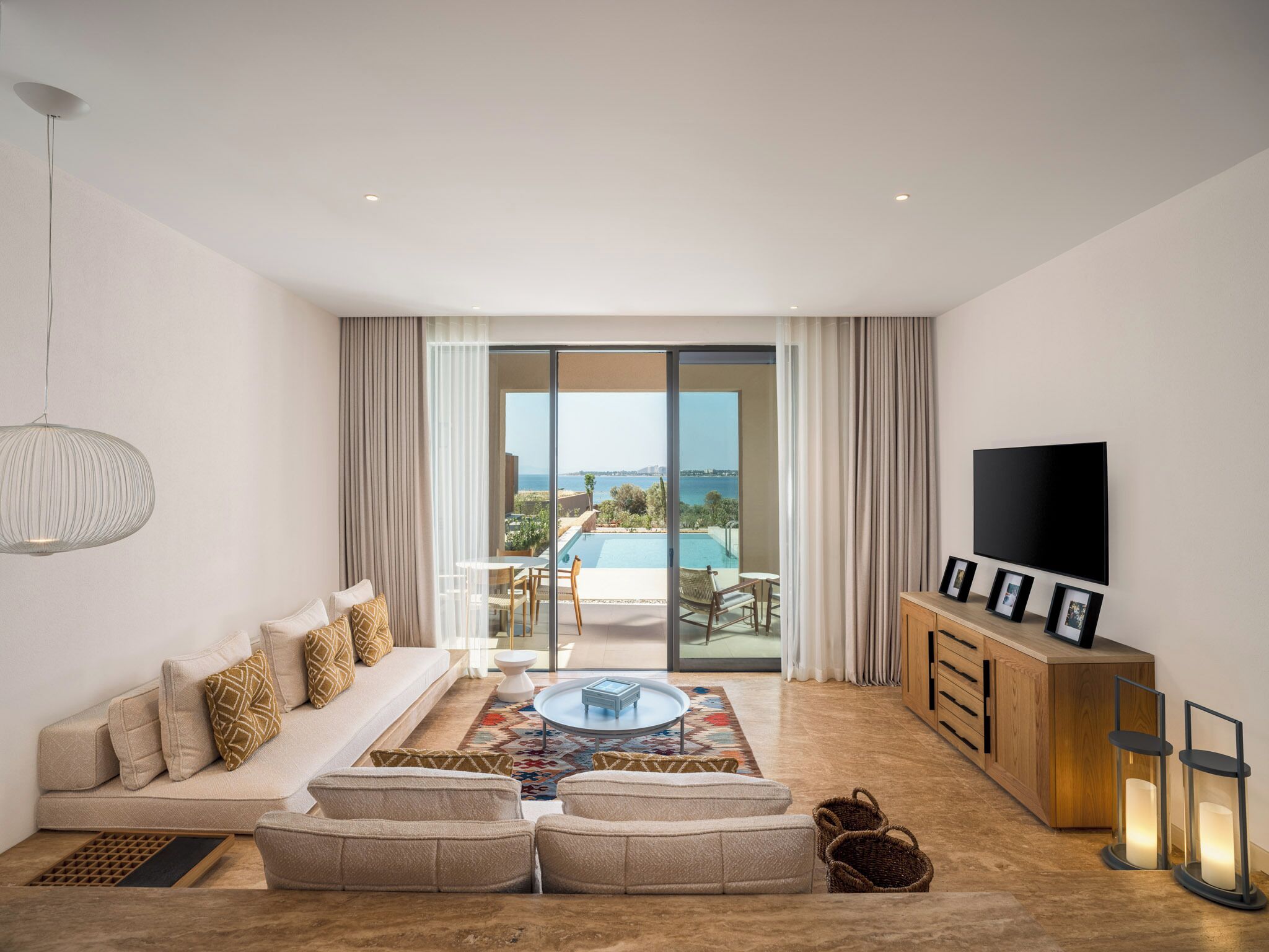 A modern living room with a sofa, a coffee table, a TV, and a view of a pool and landscape.