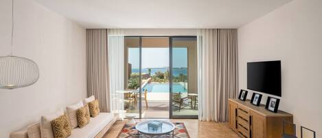 A modern living room with a sofa, a coffee table, a TV, and a view of a pool and landscape.