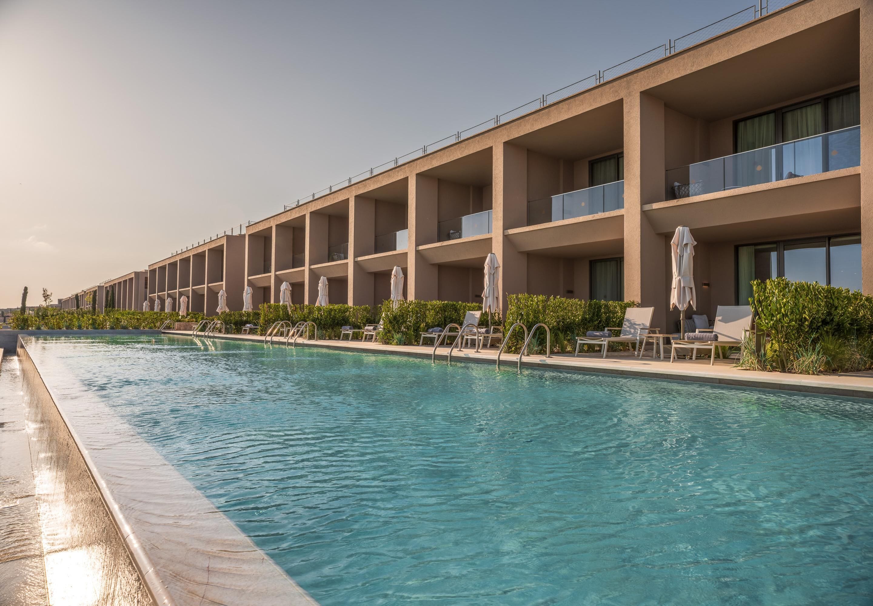 A hotel with a swimming pool, multiple balconies, and sun loungers.