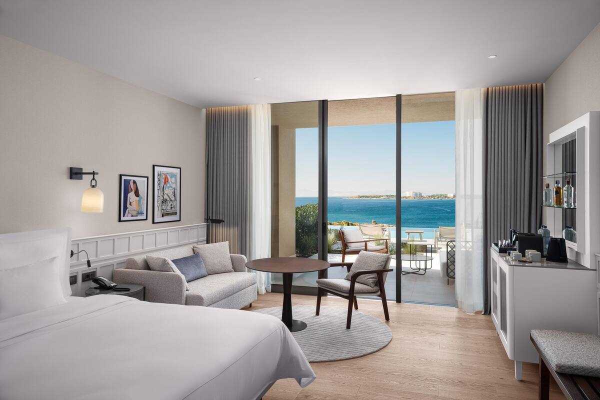 Una camera d'hotel con un letto, un divano, un tavolo da pranzo e vista sul mare.