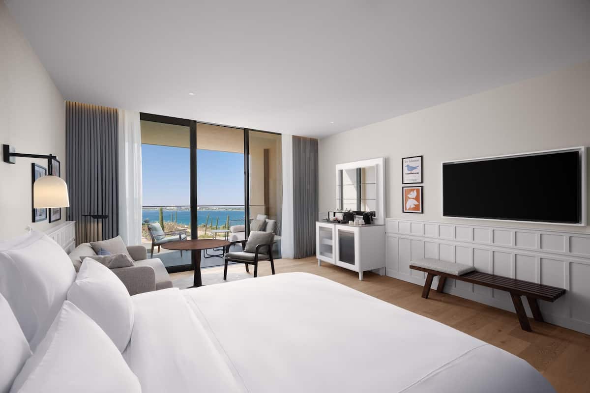 Una moderna camera d'hotel con un ampio letto, una scrivania, una sedia, una TV e vista sul mare.
