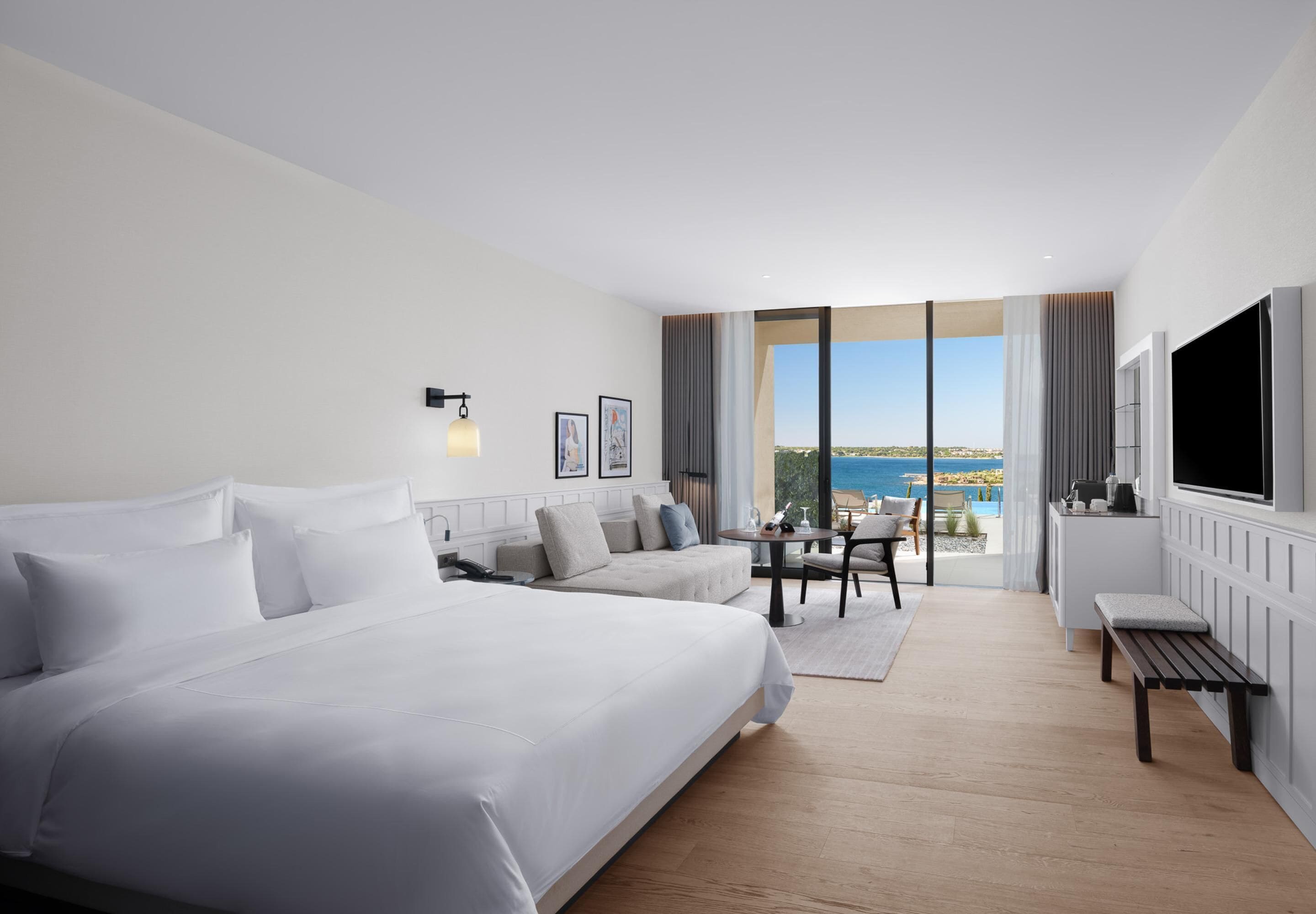 Quarto de hotel com uma cama grande, um sofá, uma mesa de jantar e uma televisão.