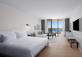 Quarto de hotel com uma cama grande, um sofá, uma mesa de jantar e uma televisão.