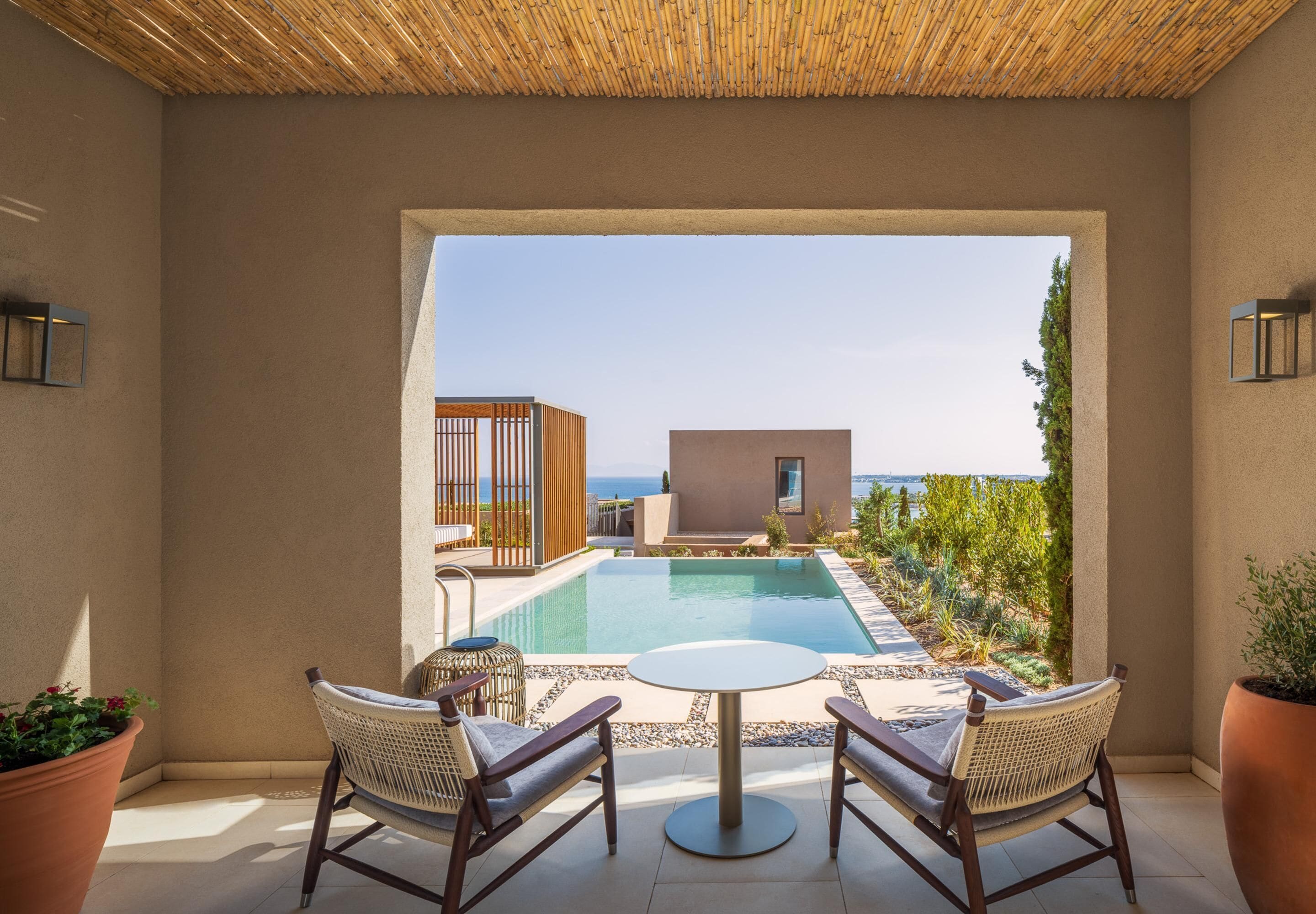A poolside area with a table and chairs, a view of the sea, and a building in the background.