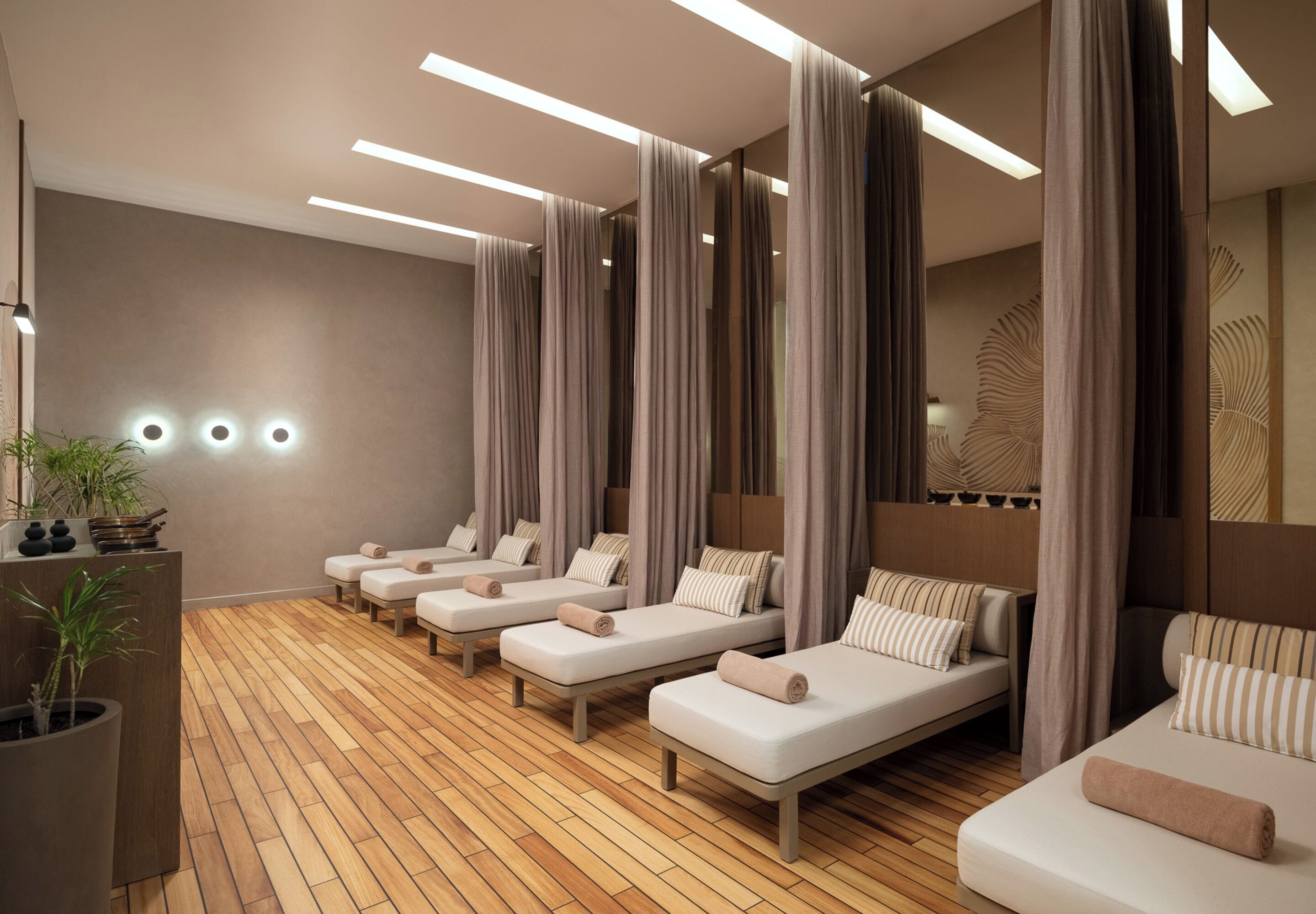A spa room with multiple massage beds, wooden flooring, and a mirror with a leaf pattern.