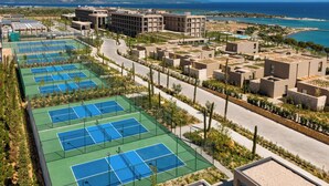 Ein Tennisplatzkomplex mit mehreren Plätzen, angrenzenden Gebäuden und Blick auf das Meer.
