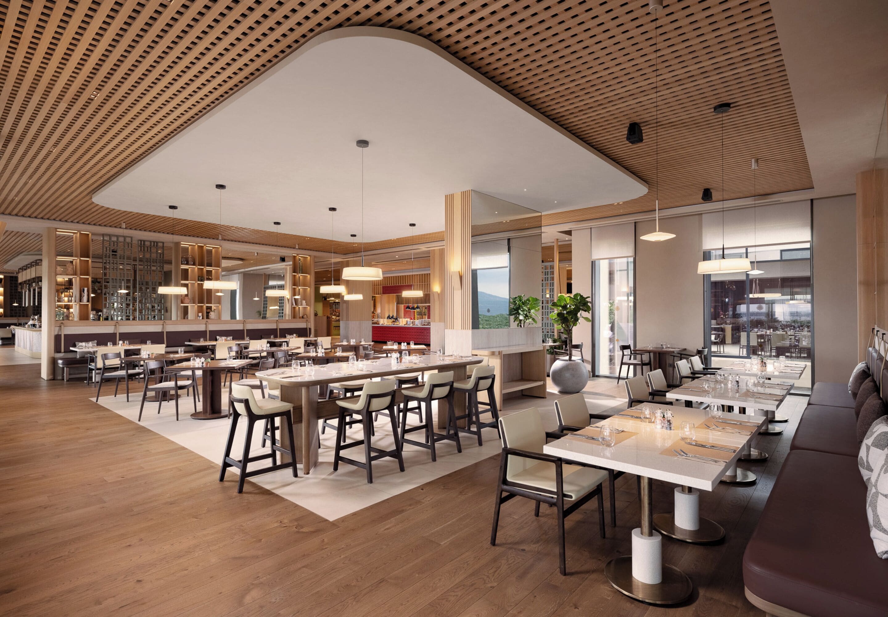 Un restaurante moderno con suelo de madera, techos altos y diversas opciones de asientos, incluyendo mesas y taburetes de bar.