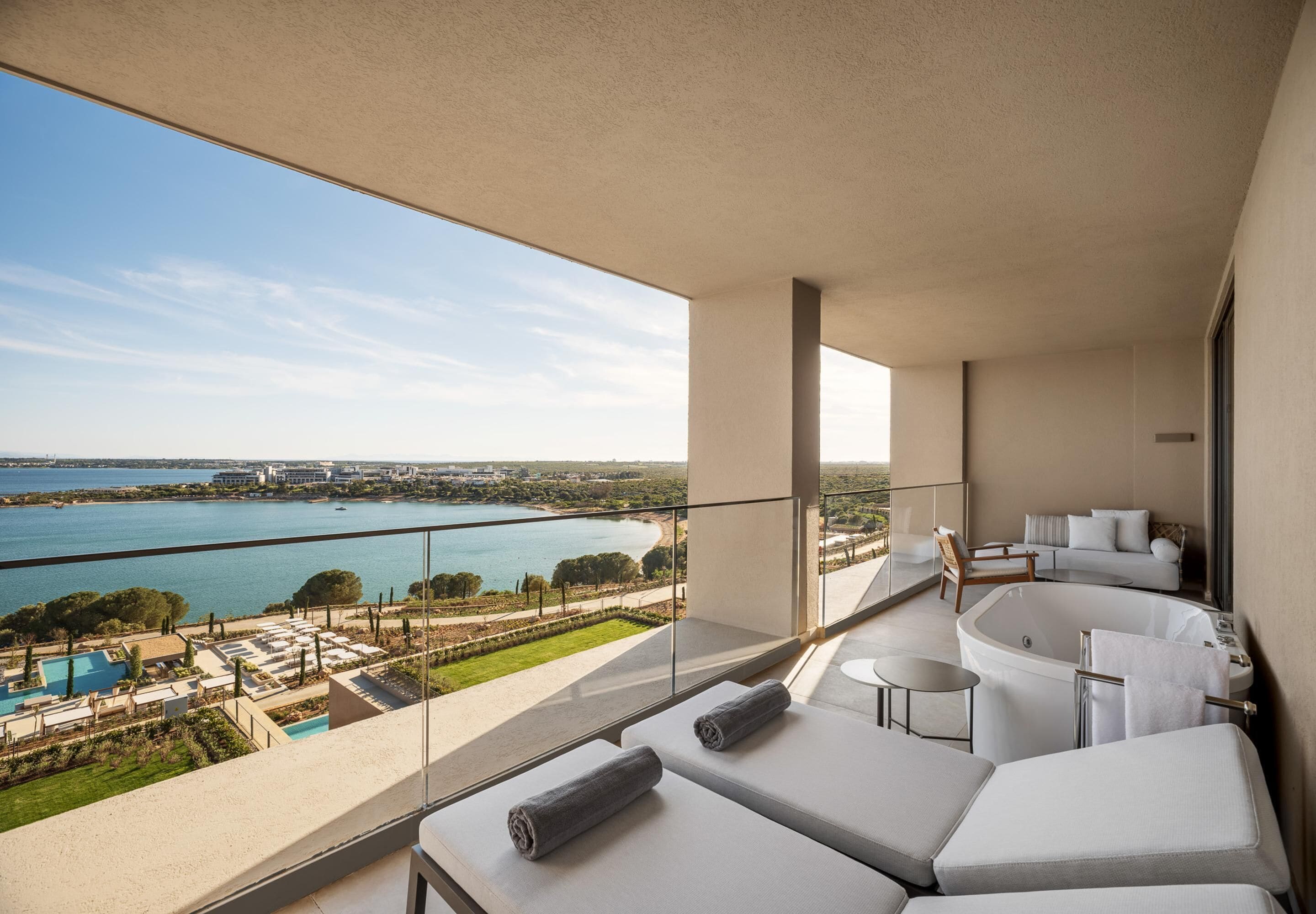Un balcón con vistas a una masa de agua, una piscina y una zona de estar con un jacuzzi.