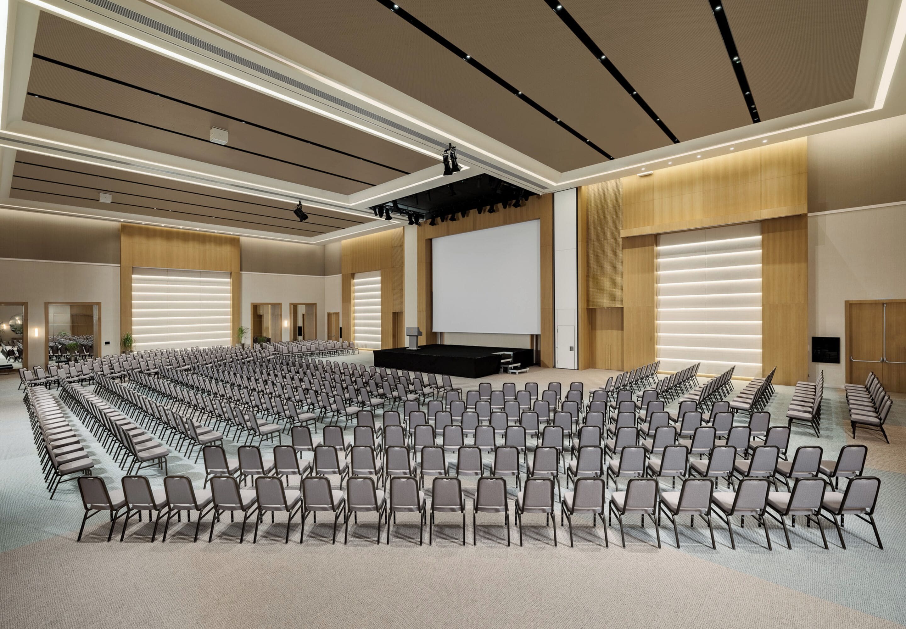 A large conference room with rows of chairs, a stage, and a large screen.
