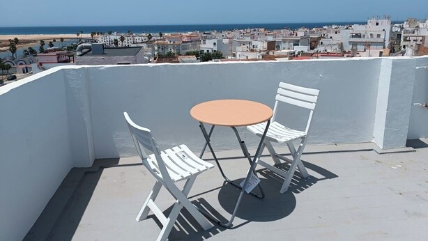 A balcony with a table and two chairs, overlooking a coastal cityscape. - Conil Beach Studio . (Conil de la Frontera)