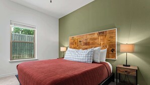 A bedroom with a bed, a window, a headboard with a wooden panel, and a nightstand with a lamp.