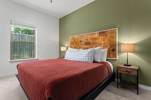 Une chambre à coucher avec un lit, une fenêtre, une tête de lit ornée d’un panneau en bois et une table de chevet avec une lampe.