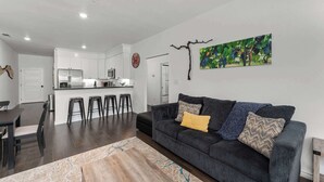A modern living room with a dark grey sofa, a coffee table, and a dining area with a table and chairs.