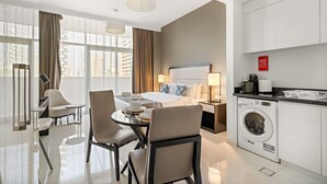 A modern hotel room with a bed, a dining area, a kitchen, and a washing machine. - Modern JVC Studio with Pool Gym and Easy Access to Attractions (Dubai)