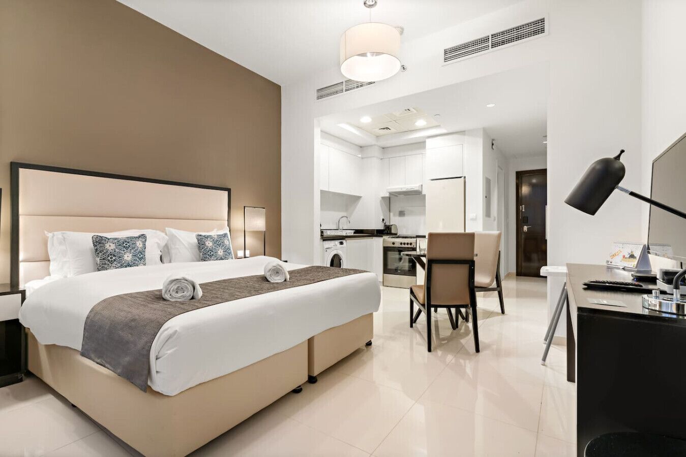 Ein modernes Hotelzimmer mit einem großen Bett, einem Schreibtisch, einem Stuhl und einer Küchenzeile.