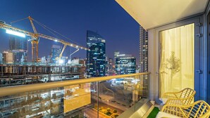Een balkon met uitzicht op de stad, twee rieten stoelen en een glazen hekwerk.