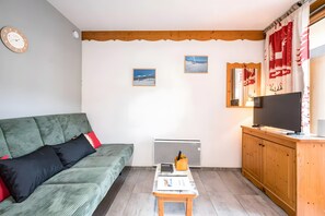 A living room with a sofa, a small table with a laptop, a TV on a wooden cabinet, and two framed pictures on the wall. - Apartment "Au refuge d'Hirka" with Mountain View, Balcony, and Wi-Fi (Val-Cenis)