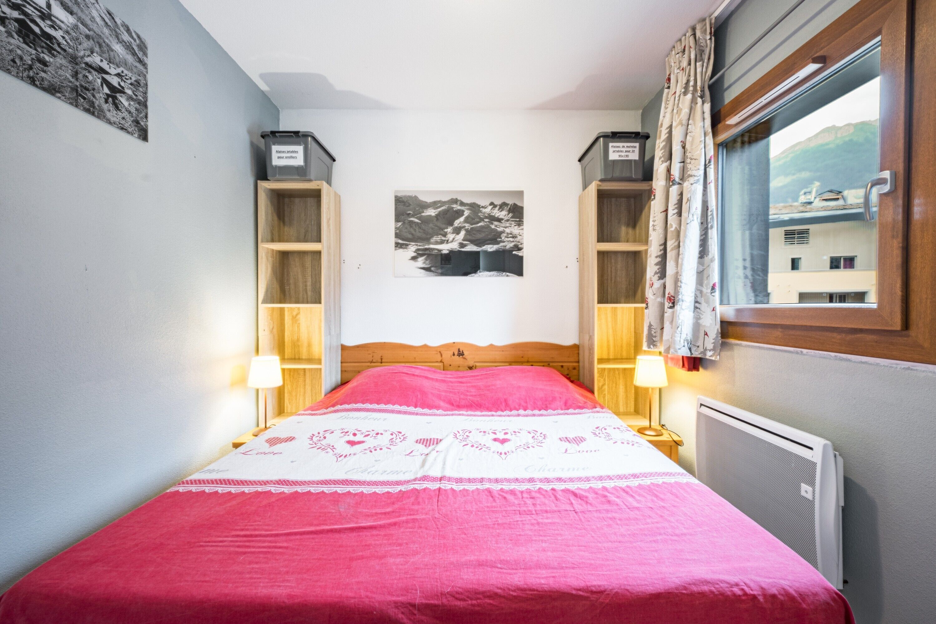 Ein Schlafzimmer mit Bett, einem Fenster mit Vorhängen, einem Heizkörper und einem Wandbild.