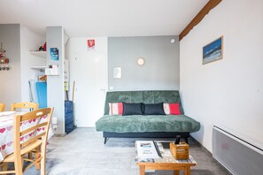 Une petite pièce agréable, avec un canapé vert, des chaises en bois, une table sur laquelle se trouve un magazine et un radiateur.