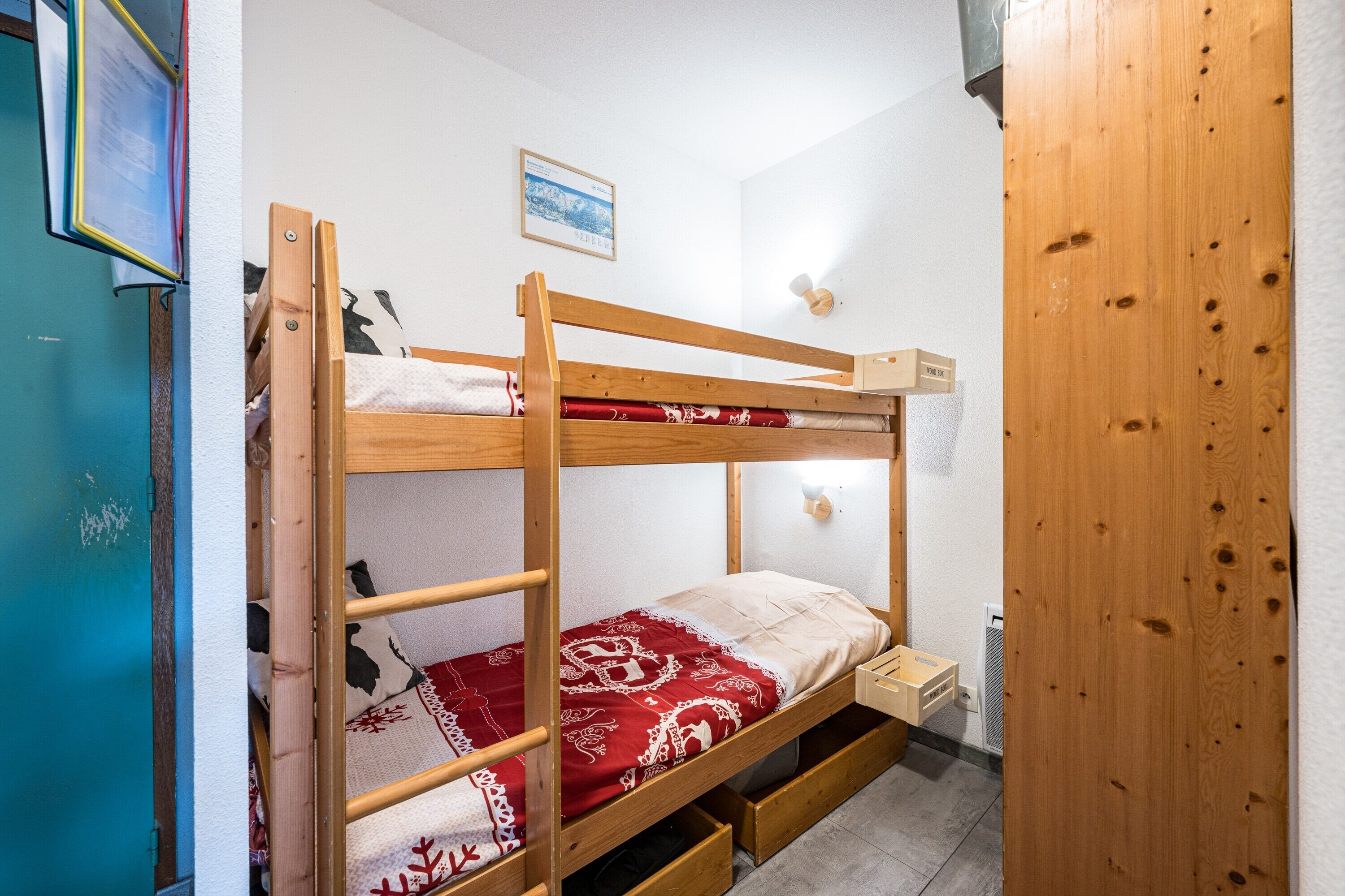 Una cama individual con ropa de cama de diseño rojo y blanco, cabecera de madera y una mesita de noche de madera.