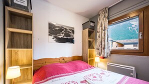 A bedroom with a bed, a nightstand, a lamp, a window with a view, and a wall-mounted shelf. - Apartment "Au refuge d'Hirka" with Mountain View, Balcony, and Wi-Fi (Val-Cenis)