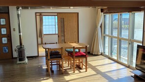 Quarto com mesa e cadeiras de madeira, um sofá e uma janela grande com cortinas.