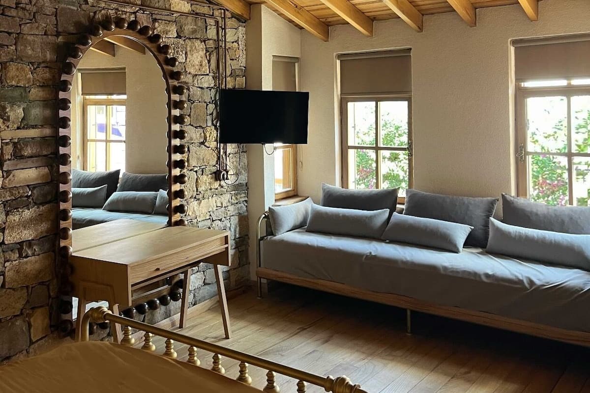 A cozy room with a stone wall, wooden ceiling beams, a bed, a sofa, and a TV.