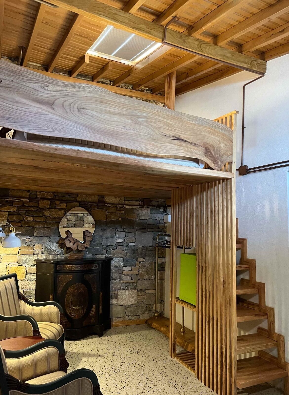 A rustic interior with a stone fireplace, wooden ceiling beams, and a staircase.
