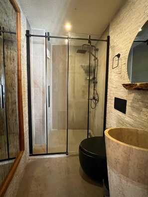A modern bathroom with a glass shower enclosure, a black toilet, and a large wooden basin. - Yaz evi bozcaada (Bozcaada)
