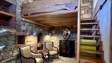 Un interior rústico con pared de piedra, vigas de madera en el techo, chimenea y escalera de madera.