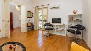 A living room with wooden flooring, a television, two black chairs, a white shelf with decorative items, and a door leading to another room. - Apartment 'Tancredi' with Mountain View, Wi-Fi and Air Conditioning (Catania)
