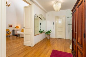 Une pièce avec un plancher en bois, une porte blanche, un miroir, une plante en pot et un tapis rouge.