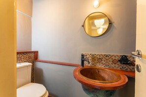 Ein Badezimmer mit Toilette, einem Holzwaschbecken, einem runden Spiegel und einer gefliesten Rückwand.