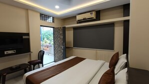 A modern hotel room with a large bed, a flat-screen TV mounted on the wall, a ceiling fan, and an air conditioning unit. - Jai Ambe Hotel (Indore)