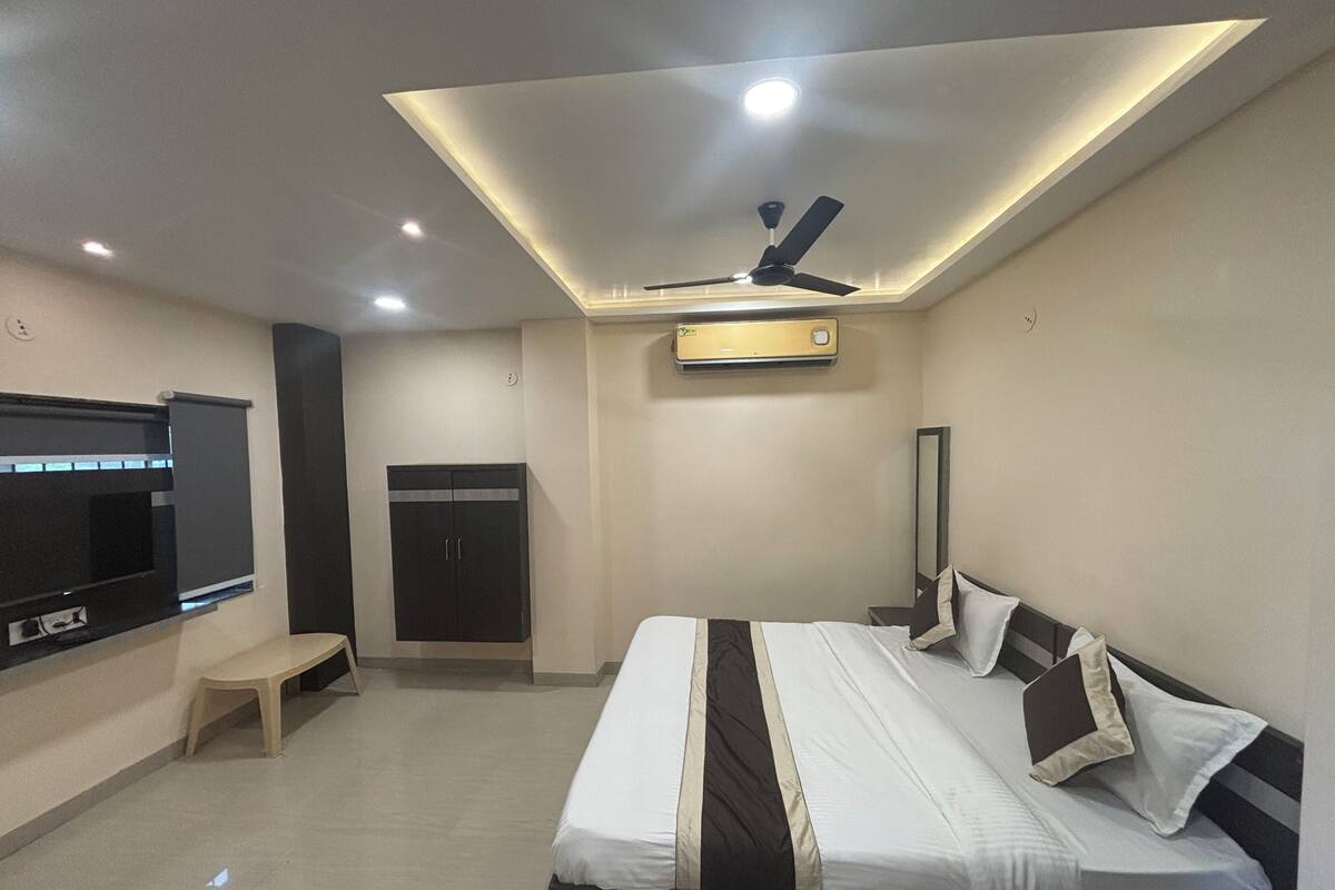 A modern hotel room with a bed, a TV, a ceiling fan, and an air conditioning unit.