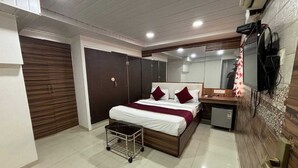 A modern bedroom with a large bed, a bedside table, a small desk, a mirror, and a wardrobe. - Hotel Lucky Galaxy (Mumbai)