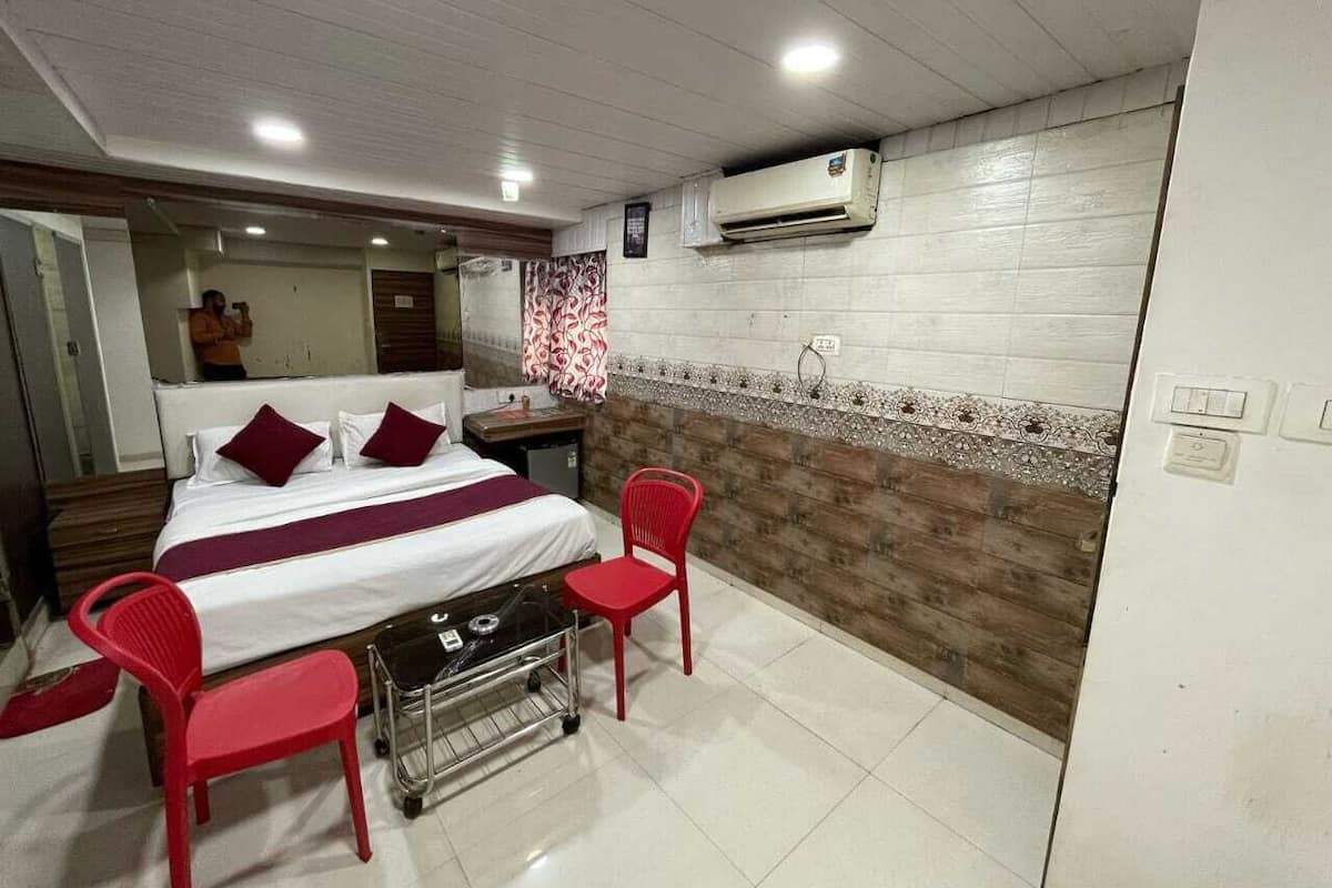 A hotel room with a bed, two red chairs, a small table, an air conditioner, and a tiled floor.