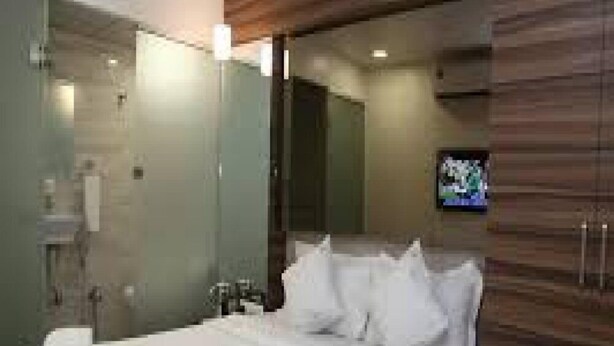 A modern hotel room with a large bed, a TV on the wall, and a bathroom with a glass shower enclosure. - Hotel Lucky Galaxy (Mumbai)