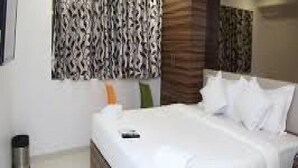 A modern hotel room with a neatly made bed, a wooden headboard, and a patterned wall above the bed. - Hotel Lucky Galaxy (Mumbai)