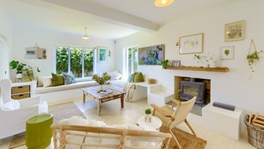 Un salon spacieux comprenant un canapé, une table basse et des fauteuils, une cheminée et de grandes fenêtres donnant sur un paysage verdoyant.