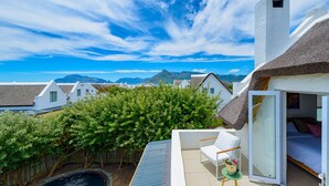 Un balcon offrant une vue sur les montagnes, des bâtiments blancs et une construction au toit de chaume.