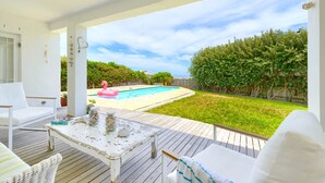 Une terrasse couverte avec une piscine, des meubles blancs et une vue sur le jardin arrière.