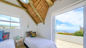 Une chambre avec deux lits, une petite table de chevet, une lampe et une vue sur la mer.