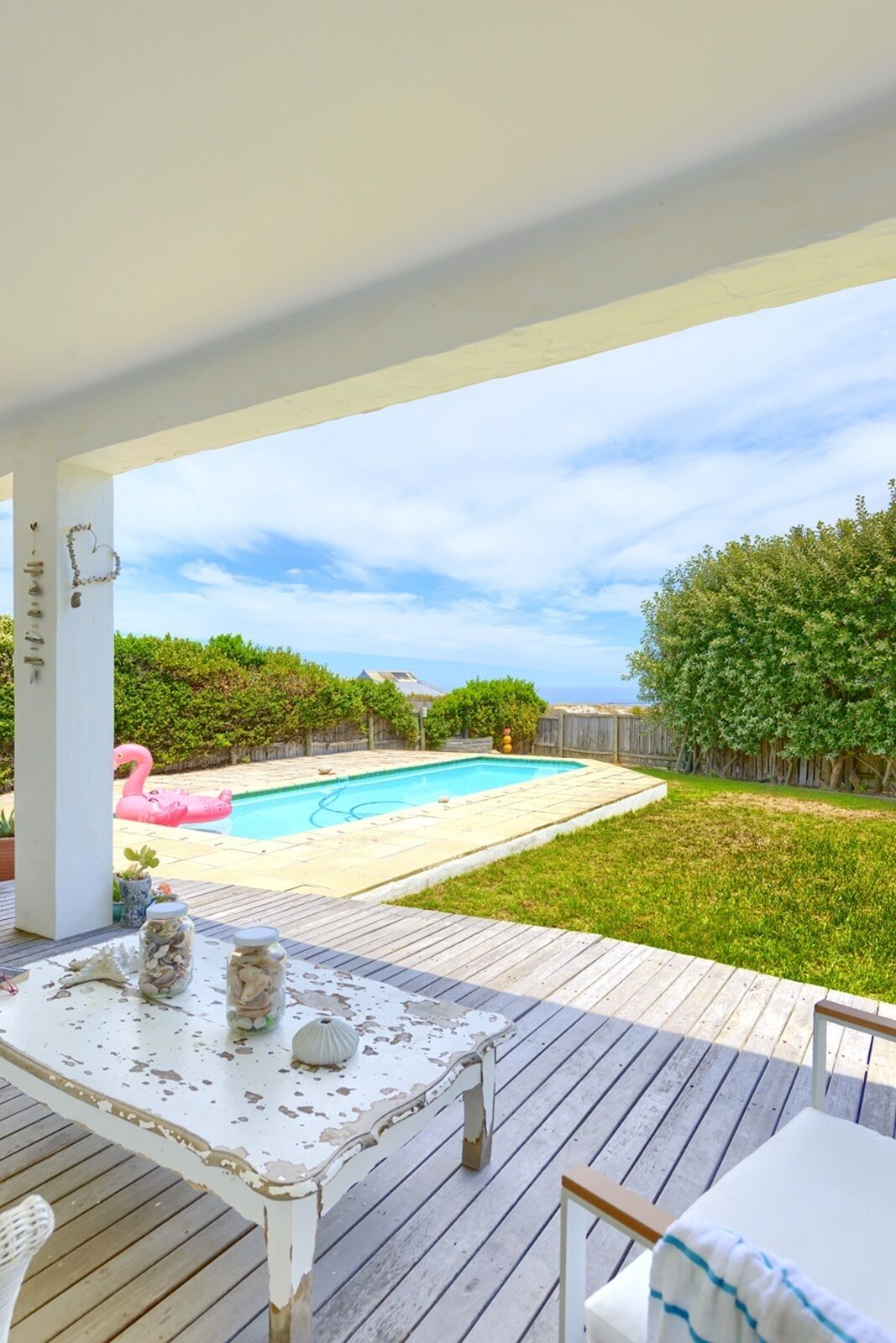 A covered patio with a pool, a table with jars, and a chair.