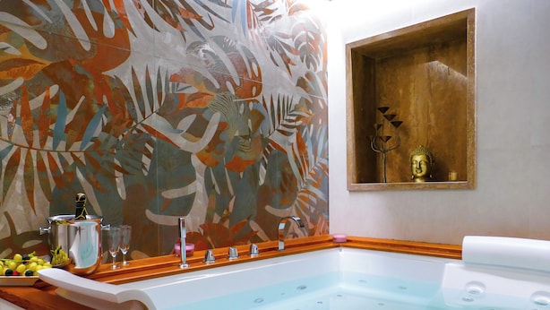 Uma casa de banho moderna com hidromassagem em vidro, uma estátua de Buda e um padrão de folha tropical na parede.
