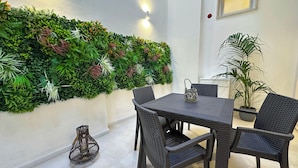 Uma área de refeições com mesa e cadeiras, uma parede decorativa com plantas e um vaso com planta.