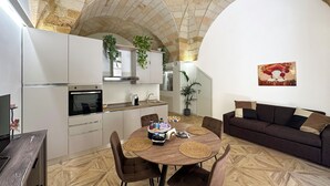 Uma sala de estar ampla com teto alto abobadado, uma mesa de jantar com cadeiras, um sofá e uma cozinha com armários brancos e arco de pedra.